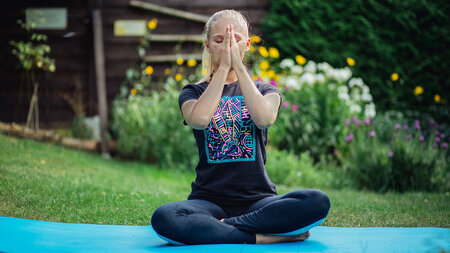 Eine Frau sitzt mit verschränkten Beinen auf einer Yoga-Matte.
