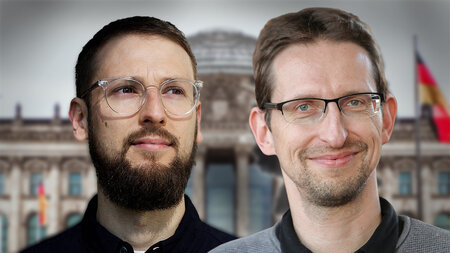 Zwei junge Männer mit Brille stehen nebeneinander. Im Hintergrund ist das Reichstagsgebäude zu sehen.