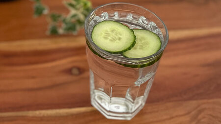 Ein Glas Wasser mit Gurkenscheiben steht auf einem Tisch.