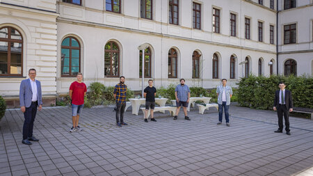 Zwei Männer mittleren Alters und fünf junge Männer stehen nebeneinander.