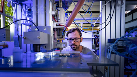 Ein Mann schaut in den Maschinenraum des 3D-Druckers, in dem gedruckte Bauteile liegen. 
