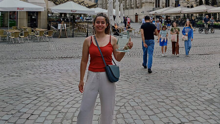 Eine junge Frau steht auf einem Markplatz und hält eine Trophäe in der Hand. 