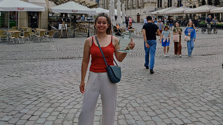 Eine junge Frau steht auf einem Markplatz und hält eine Trophäe in der Hand. 