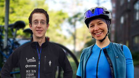 Eine junge Frau in Rennradkleidung und ein junger Mann mit Brille stehen nebeneinader und lächeln.