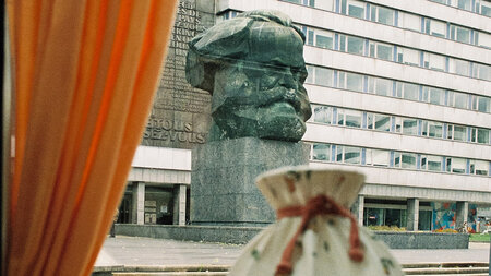 Das Chemnitzer Karl-Marx-Monument durch eine Scheibe mit Vorhang gesehen.