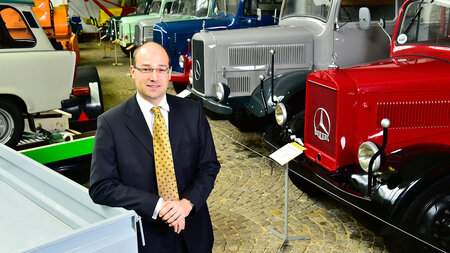 Ein Mann im Anzug steht in einer Oldtimer-Ausstellung.