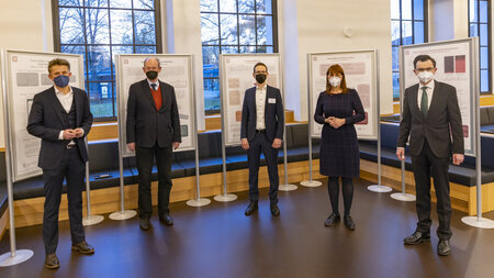 Mehrere Personen mit Maske stehen vor einer Posterausstellung.