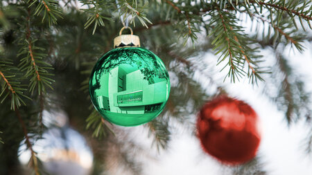 An einem Tannenzweig hängt eine grüne Weihnachtskugel, in der sich ein Gebäude spiegelt.