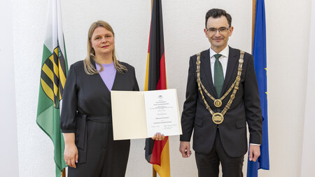 Eine Frau und ein Mann stehen nebeneinander. Die Frau hält eine Urkunde.