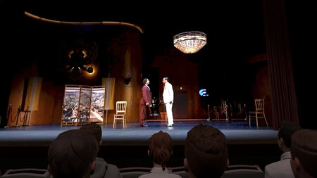 Blick auf eine reale Opernbühne, auf der zwei Personen mit einander reden. Avatare im virtuellen Zuschauerraum beobachten sie dabei.