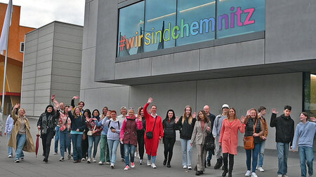 Eine Gruppe steht vor einen Gebäude. Auf eines der Fenster ist der Schriftzug "Wir sind Chemnitz" angebracht.