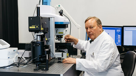 Ein Mann im weißen Kittel arbeitet in einem Labor an einem Mikroskop.