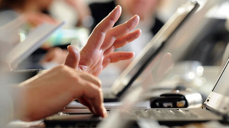 Eine Hand liegt auf der Tastaur eines Laptops auf. 
