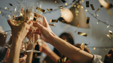 A toast is raised with champagne glasses and confetti flies through the air. 