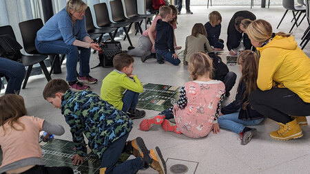 Mehrere Kinder hocken rund um Spielpläne auf dem Boden.