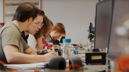 Mehrere Schüler sitzen nebeneinander an einem Labortisch und experimentieren. 