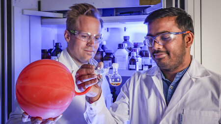Zwei Chemiker halten in einem Labor eine Vorrichtung in der Hand.