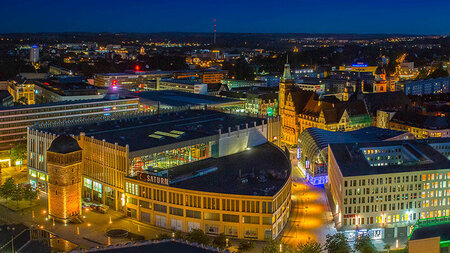 Blick aus der Vogelperspektive auf mehrere beleuchtete Gebäude bei Nacht.