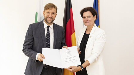 Zwei nebeneinander stehende Männer halten eine Urkunde in den Händen.