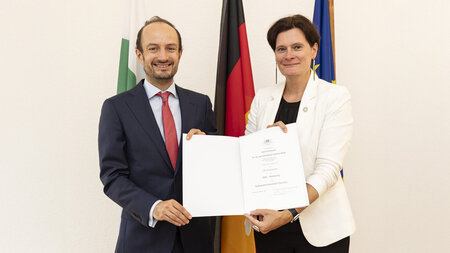 Zwei Männer stehen nebeneinander und halten eine Urkunde in den Händen.