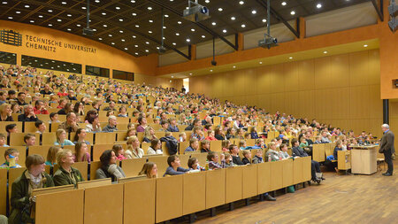 Ein Mann steht vor einem vollbesetzten Hörsaal.