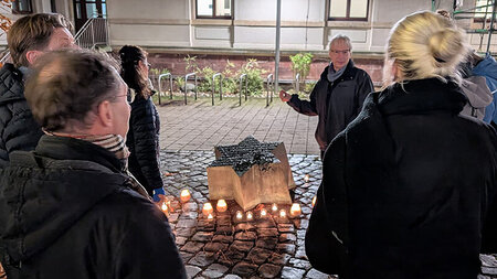 Ein Mann steht neben einem sternförmigen Gedenkstein und spricht zu mehreren Personen.