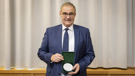 Ein Mann im Anzug hält eine Schatulle mit einer weißen Medaille in den Händen.