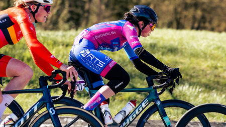 Eine Frau im Sportdress hält ein Fahrrad fest.