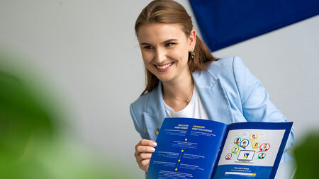 Eine lächelnde junge Frau hält eine Publikation in den Händen. 