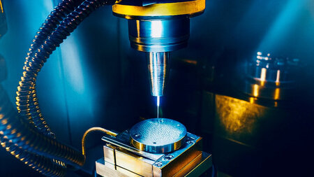 Ein dünner Bohrer rotiert über einem Werkstück. 