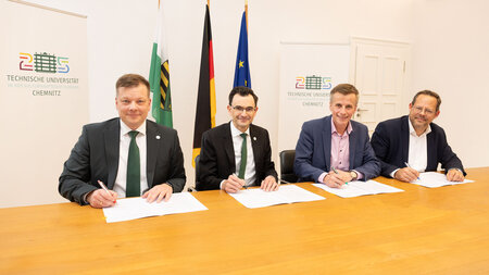 Vier Männer sitzen an einem Tisch und unterzeichnen Dokumente.