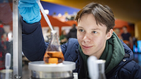 Ein junger Mann experiementiert an einem Glasgefäß mit einer Flüssigkeit. 