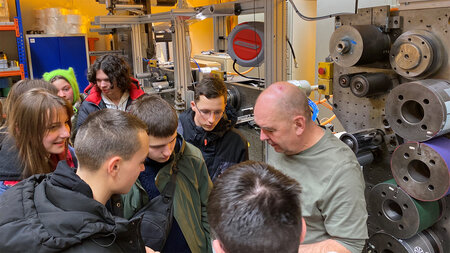 Ein Mann steht mit jungen Leuten neben einer Druckmaschine.