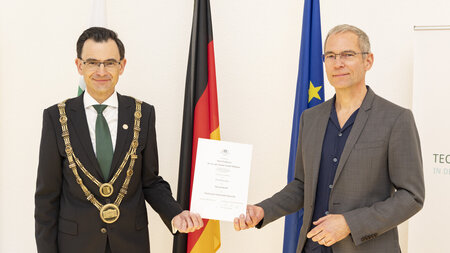 Zwei Männer stehen nebeneinander und halten eine Urkunde in den Händen. 