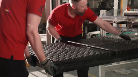 Zwei Männer greifen nach einem plattenförmigen Bauteil um es aus einer Maschine zu heben. 