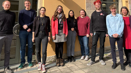 Mehrere Personen stehen nebeneinander vor einer Hauswand.