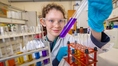 Mädchen steht vor einem Schraubstock und bearbeitet ein Metallstück