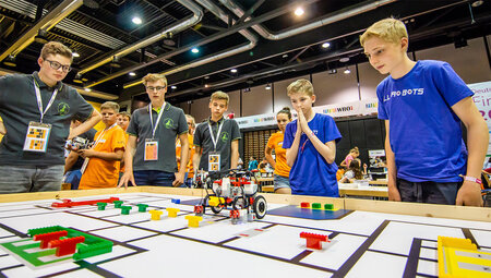 Mehrere Schüler stehen um einen Tisch herum, auf dem ein kleiner Roboter einen Parcour abfährt.
