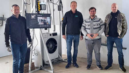 Vier Männer stehen neben einer Waschmaschine.