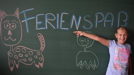 Ein Mädchen steht an einer Tafel, auf der Ferienspaß steht.