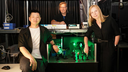 A woman and two men are standing at an experimental setup in a dark laboratory.