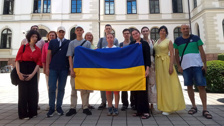 Several people are standing side by side, holding a blue-and-yellow flag in their hands