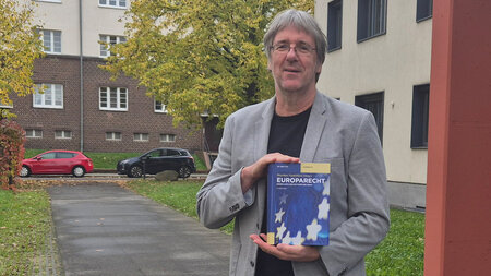 Ein Mann steht vor einem Gebäude und hält ein Buch in den Händen.