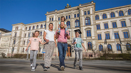 Parents with three chilfrens are walking in front of the university main building. 