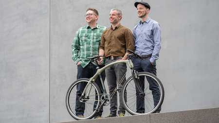3 men stand behind a bicycle. 