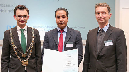 A group of three people, including a person, who is holding a certificate 