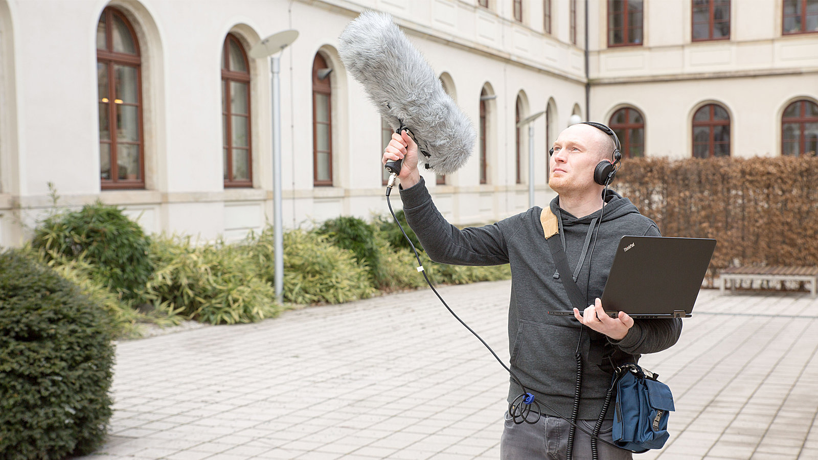Mann mit Mikrofon und Laptop steht im Innenhof der TU Chemnitz