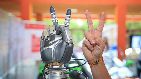 Hands of robot and human shows the victory gesture.