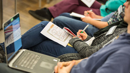 Mehrere Personen mit Laptop sitzen in einem Hörsaal.