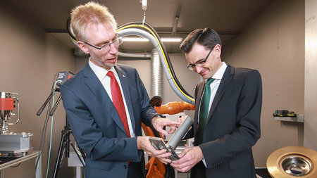 Prof. Lampke and Prof. Strohmeier discuss a small turbine blade that they are holding in their han